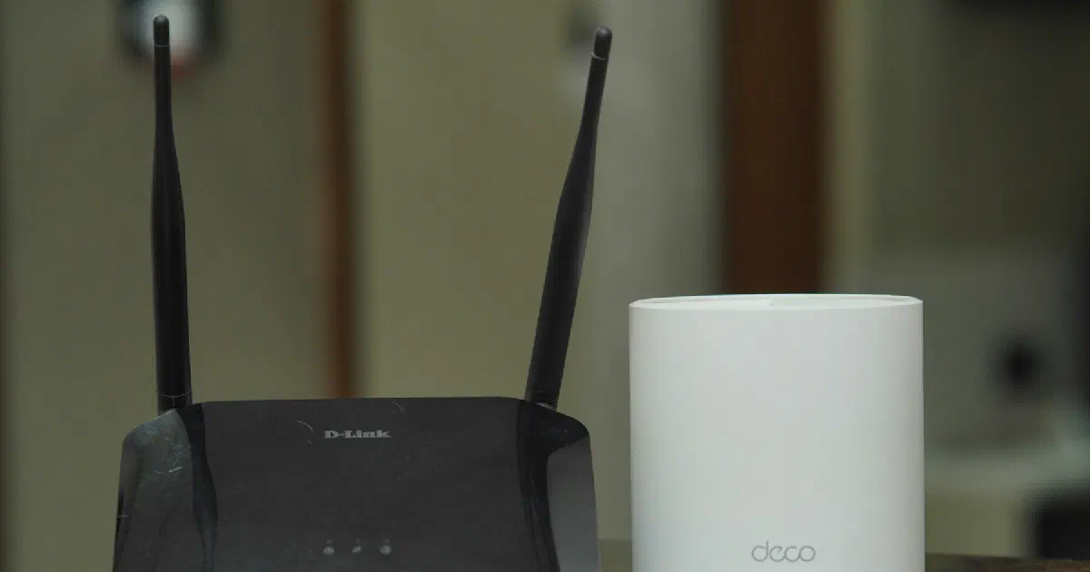 Black Wi-Fi router next to a white TP-Link Deco mesh unit on a table