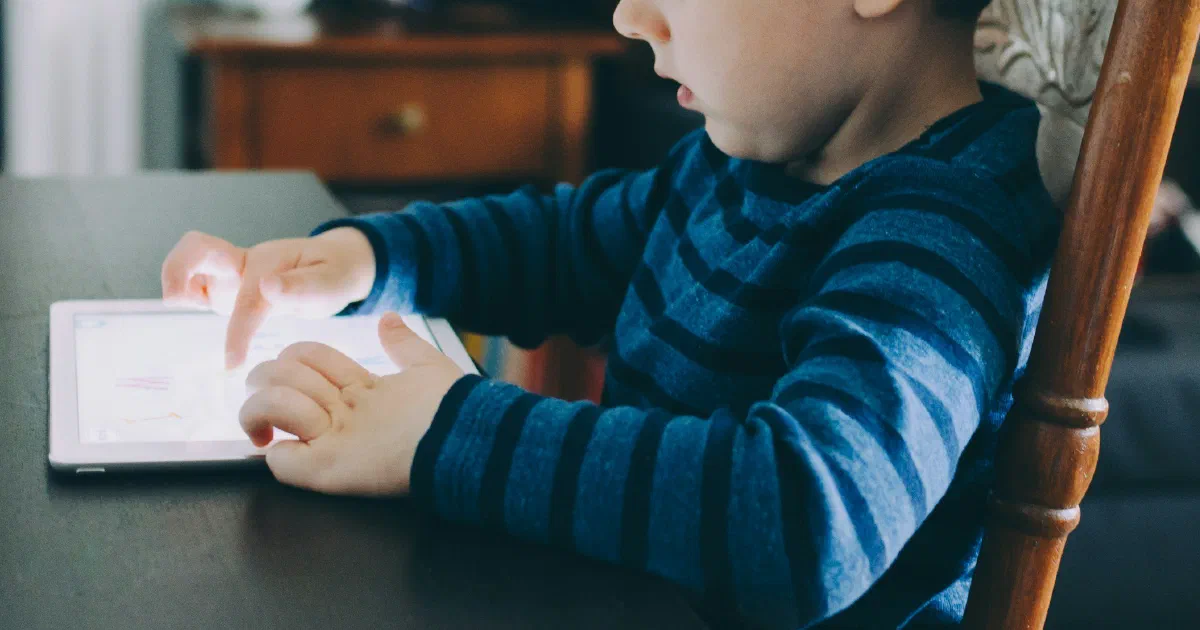 A young child in a striped shirt tapping a white tablet on a dark wooden table