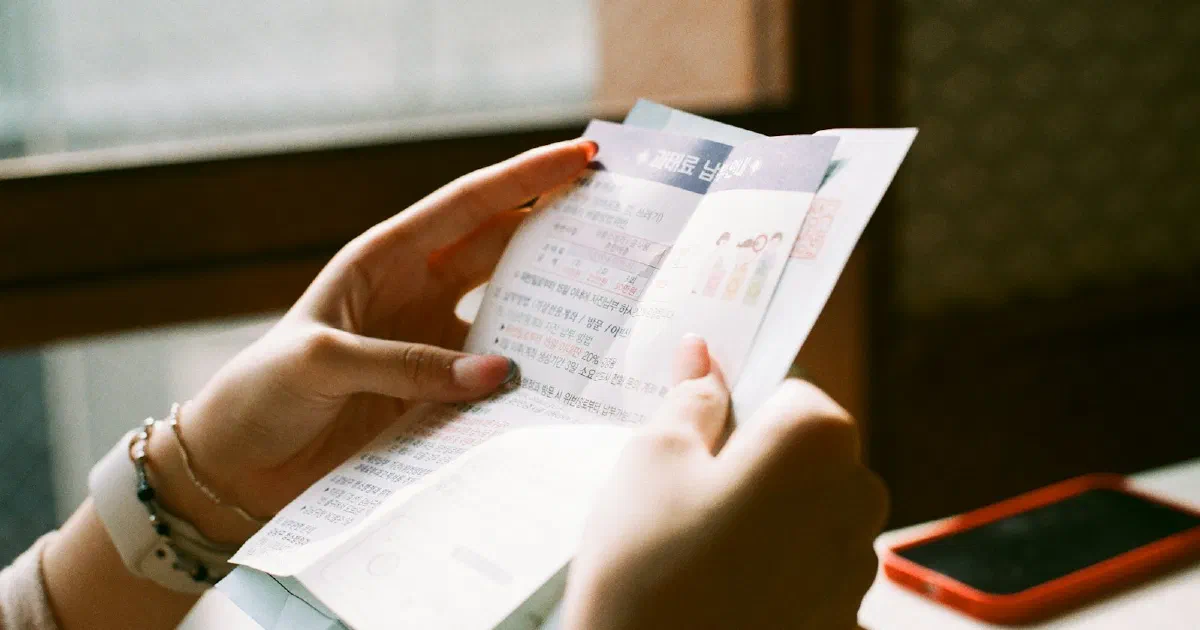 Person reading a printed bill at a table beside a phone