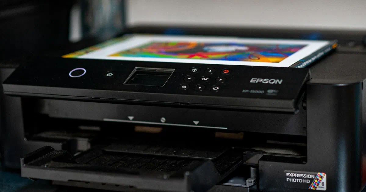 Black Epson inkjet printer with a colorful print on its top tray, sitting on a metal shelf