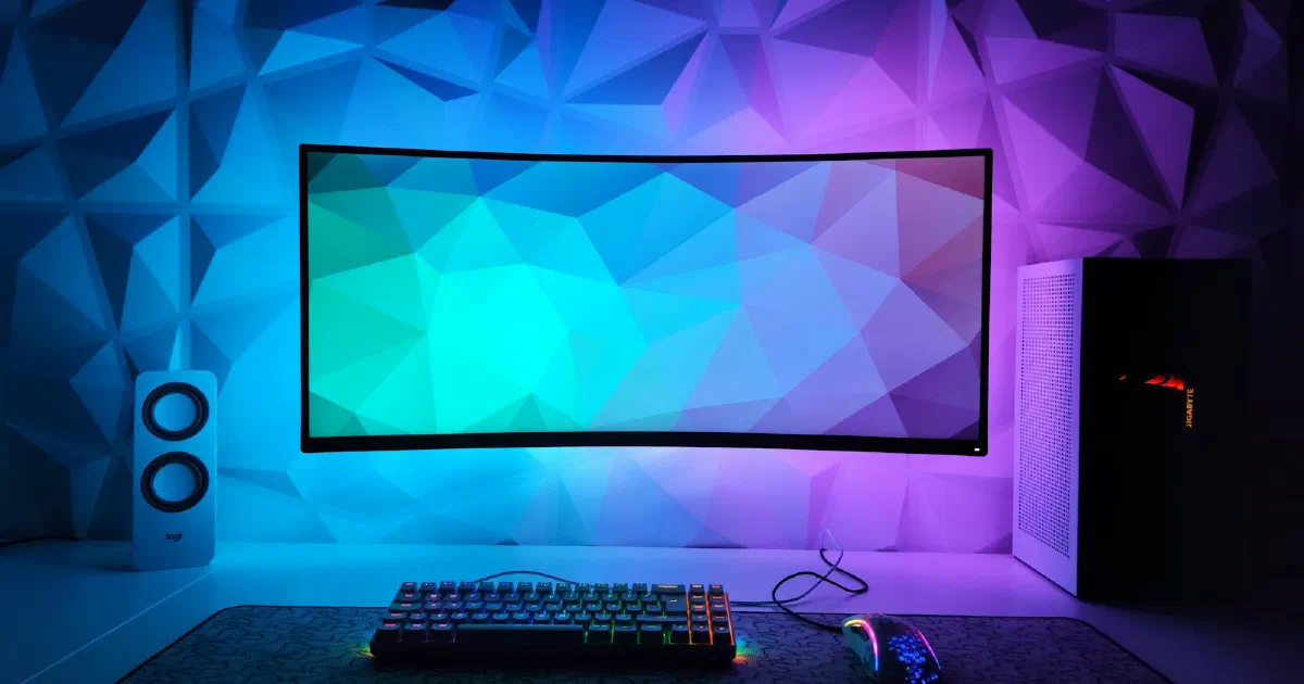 Gaming desk with a curved monitor, keyboard and purple and blue lighting