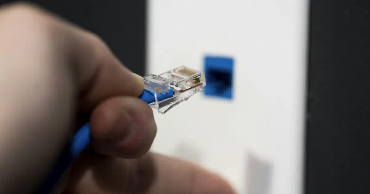 Hand plugging an Ethernet cable into a wall network jack
