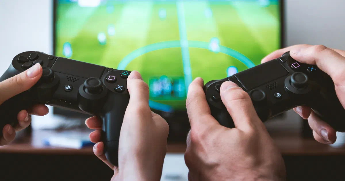 Two people holding game controllers while playing a soccer game on a TV