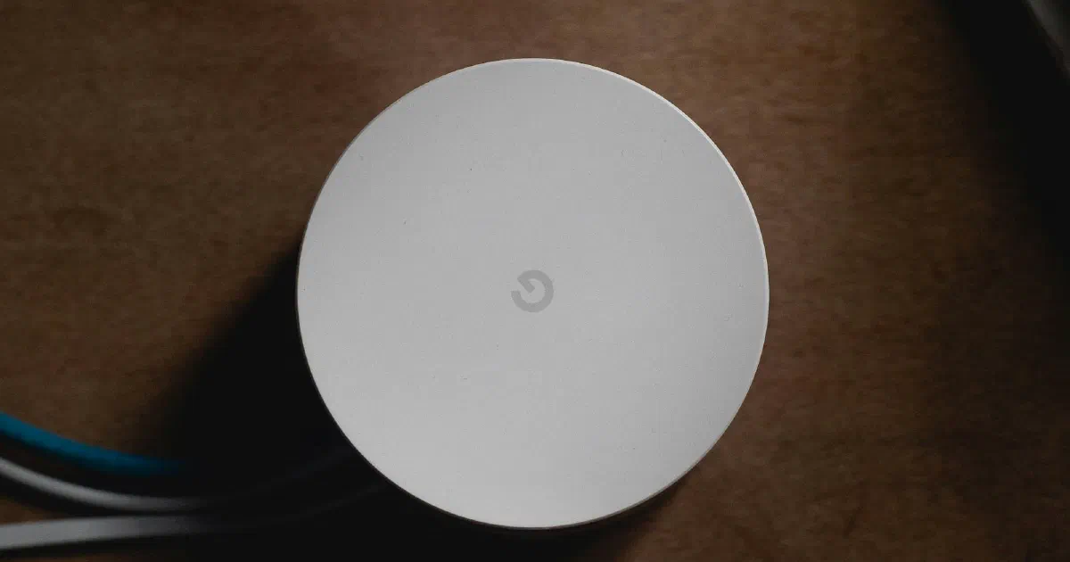 Top-down view of a round white Google Wi-Fi unit with cables attached, on a brown wooden surface