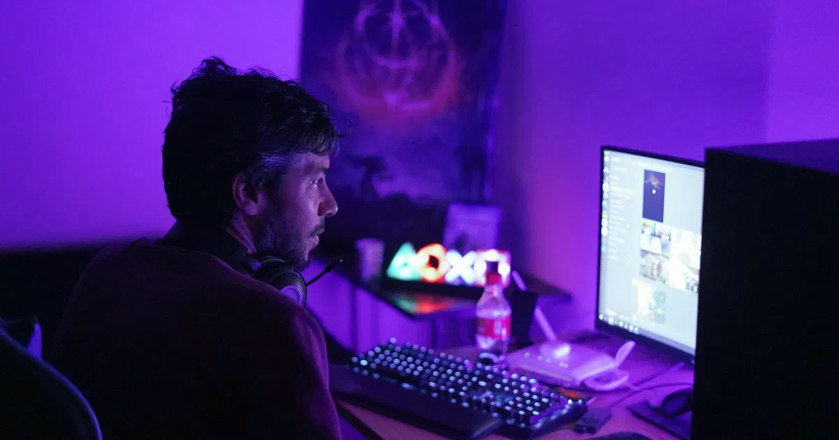 Man wearing a headset plays a game at a desktop PC with a mechanical keyboard in a room lit purple