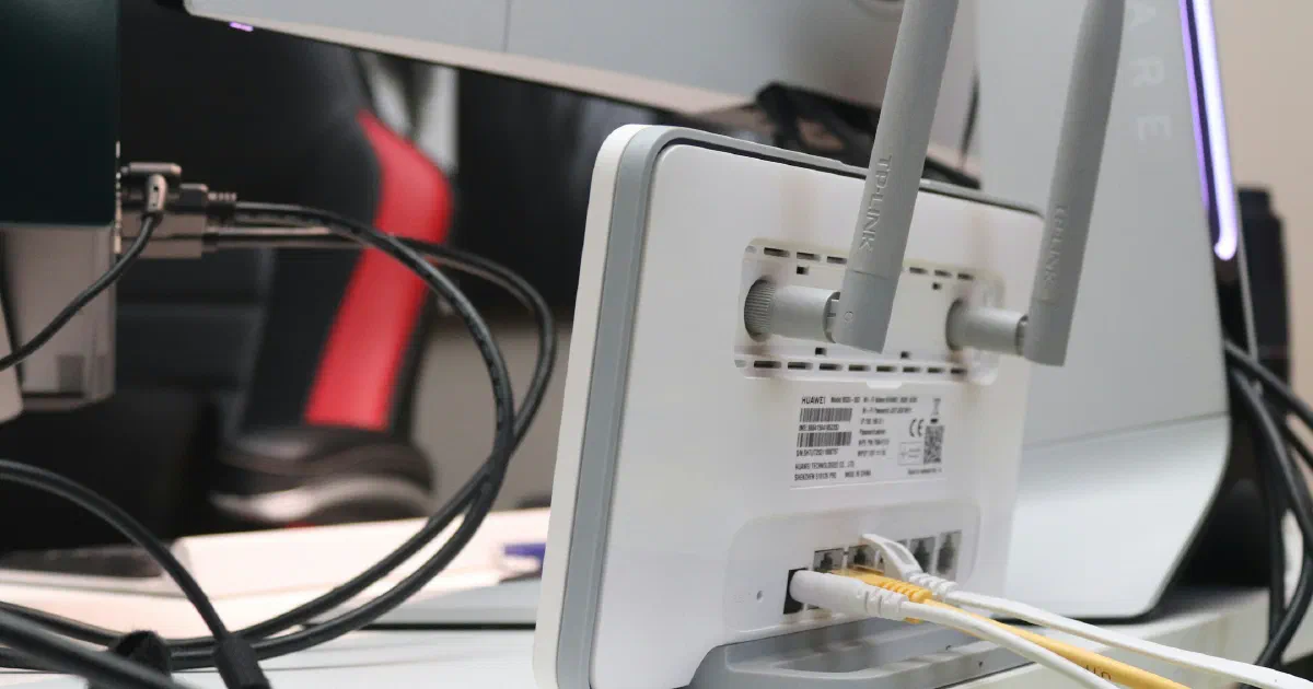 The back of a white router with two antennas and Ethernet cables plugged in, next to a computer monitor