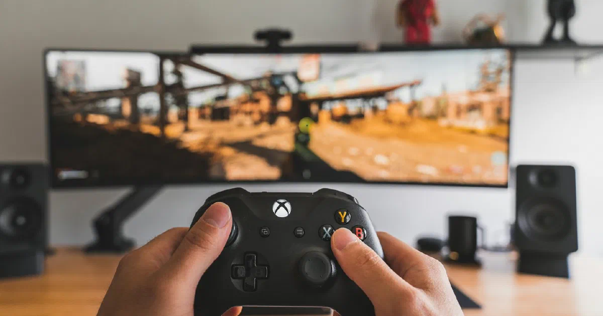 Hands holding a game controller in front of a monitor showing a game