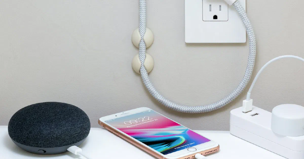 Smart speaker and smartphone charging on a white table, plugged into a power strip below a wall outlet
