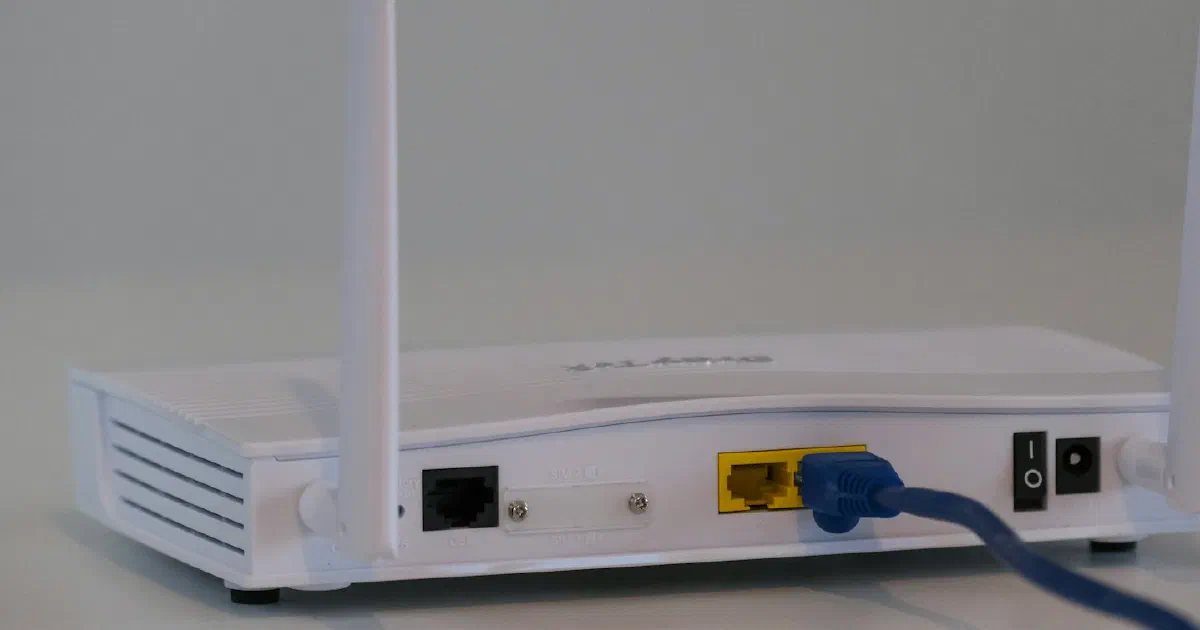 Back of a white Wi-Fi router with two antennas and an Ethernet cable plugged in