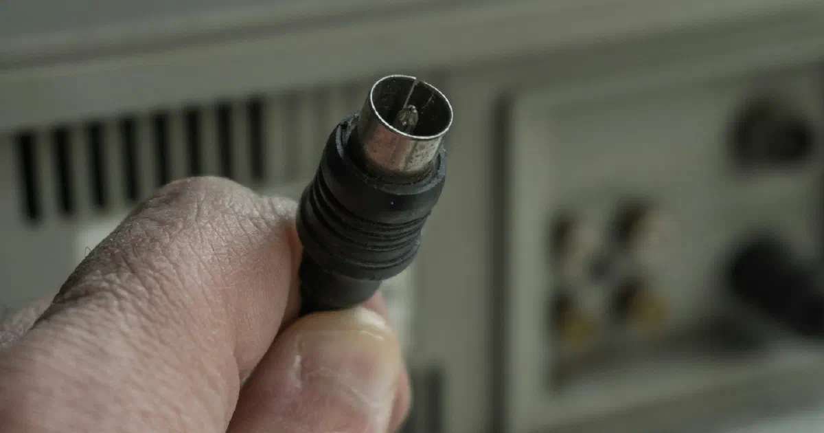 Hand holding a coaxial TV cable connector near the back of a device