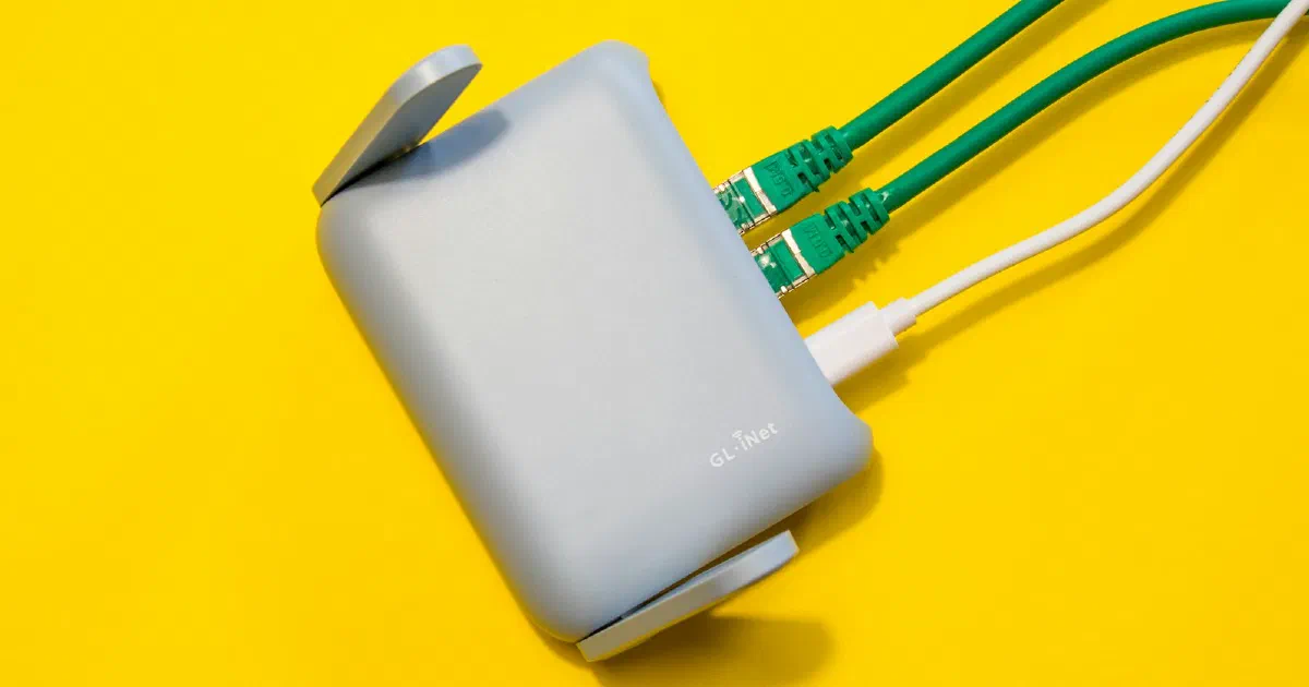 Small gray router with green Ethernet cables plugged in, on a yellow background