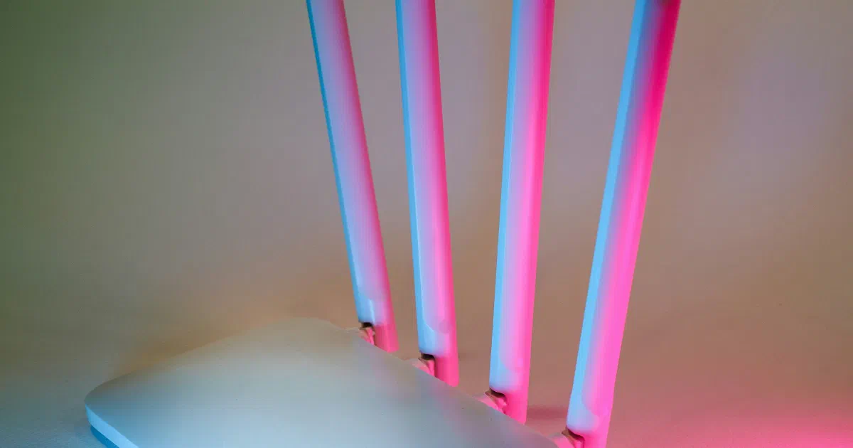 A white Wi-Fi router with four tall antennas lit by blue and pink light